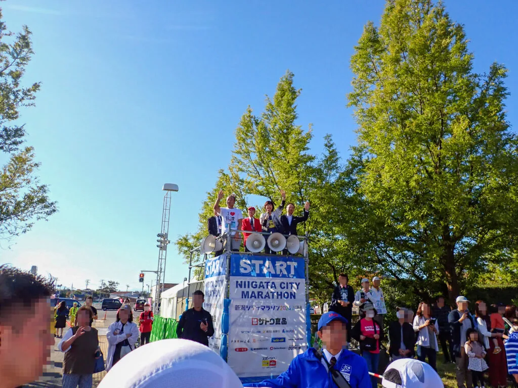 「START」の看板を掲げたスタート台と、挨拶を見守る人たち