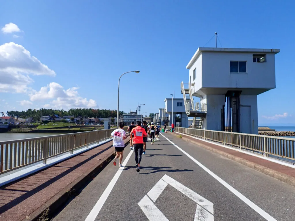 水門の操作室が建つ新潟大堰橋の上を走るランナーたち