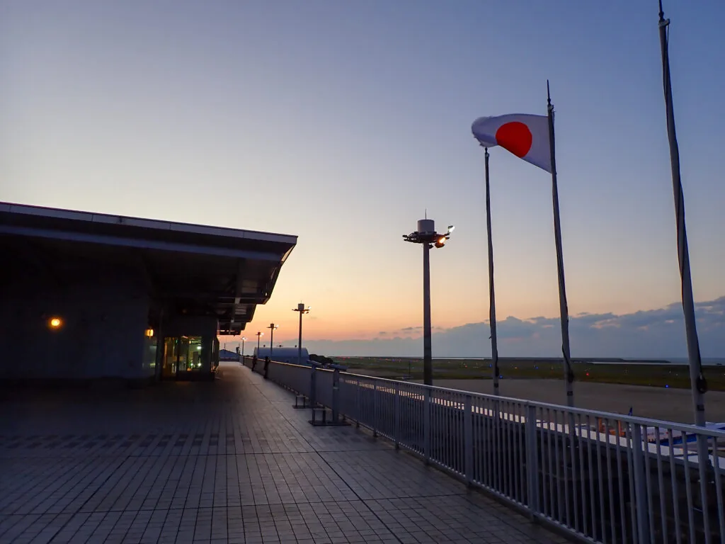 夕焼けの空に日の丸がたなびく、建物脇の広い通路