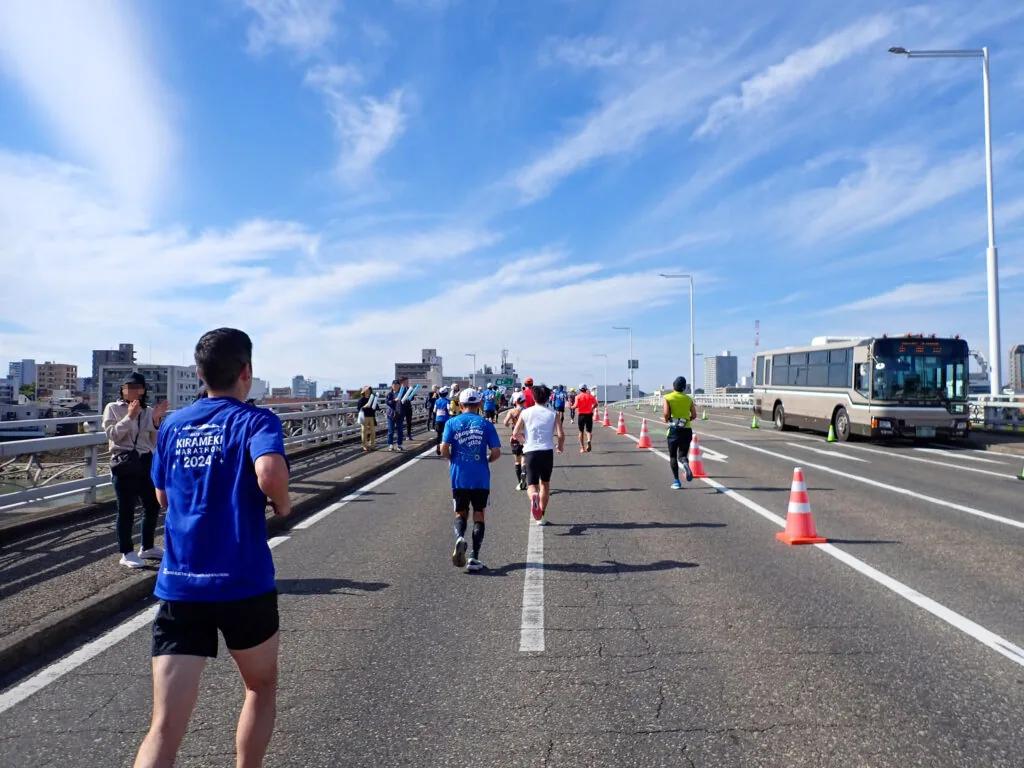新鶴見橋を渡るランナーたちと、遠くに見える市街地のビル