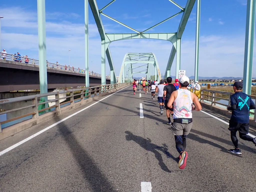 淡い緑の鉄骨が組まれた倉敷川橋を渡るランナーたち