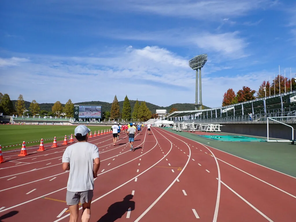 照明塔と電光掲示板が見える競技場の赤いトラックに戻ってきたランナーたち