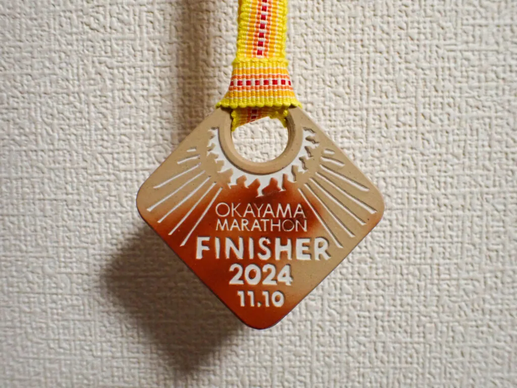 「FINISHER 2024」と刻まれた、黄色いリボン付きのひし形の完走メダル