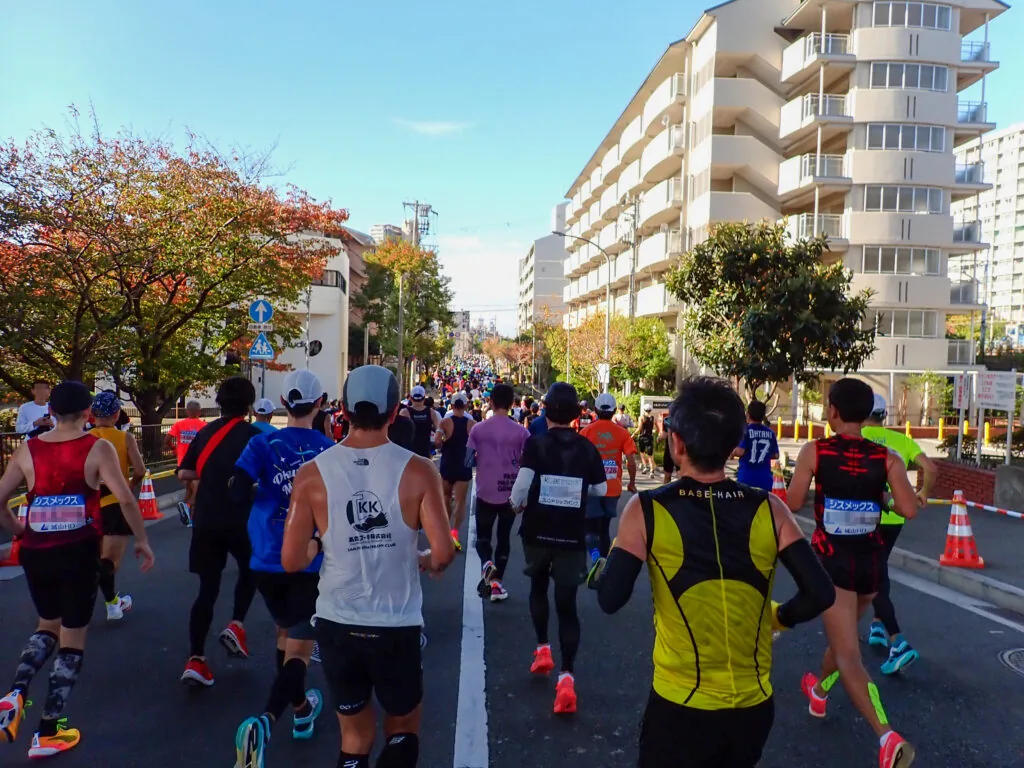 紅葉した街路樹と白い集合住宅が並ぶ道を走るランナーたち