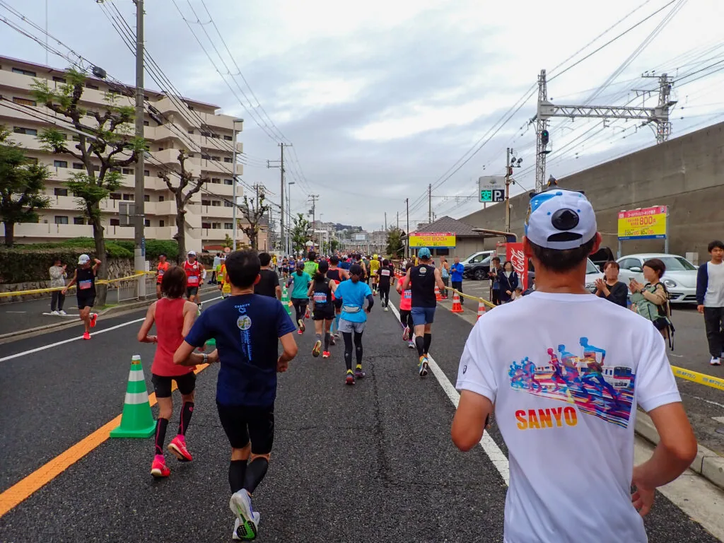 集合住宅と電線が連なる道を、折り返して東へ戻るランナーたち