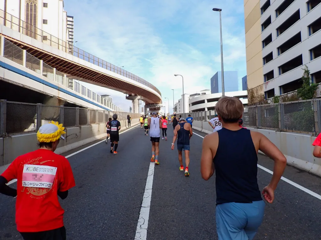 高架の道路とビルの間の登り坂を、ポートアイランドへ向かうランナーたち