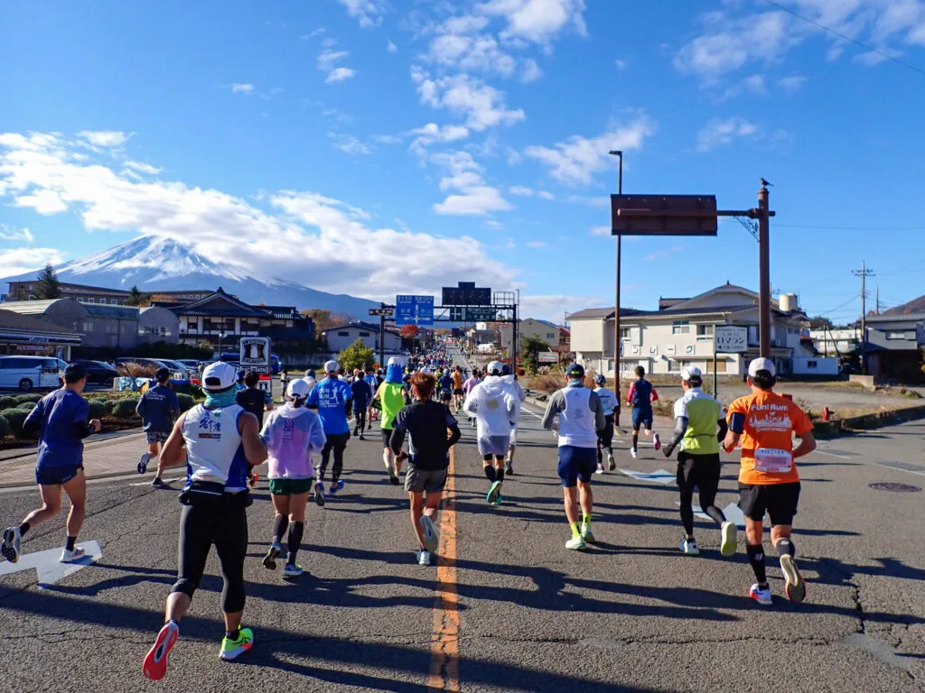 雪をかぶった富士山を遠くに望む街なかの道を走るランナーたち