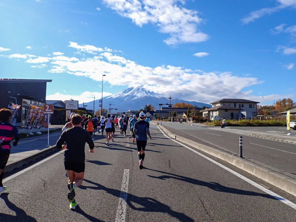 沿道の建物の向こうに富士山がそびえる道を走るランナーたち