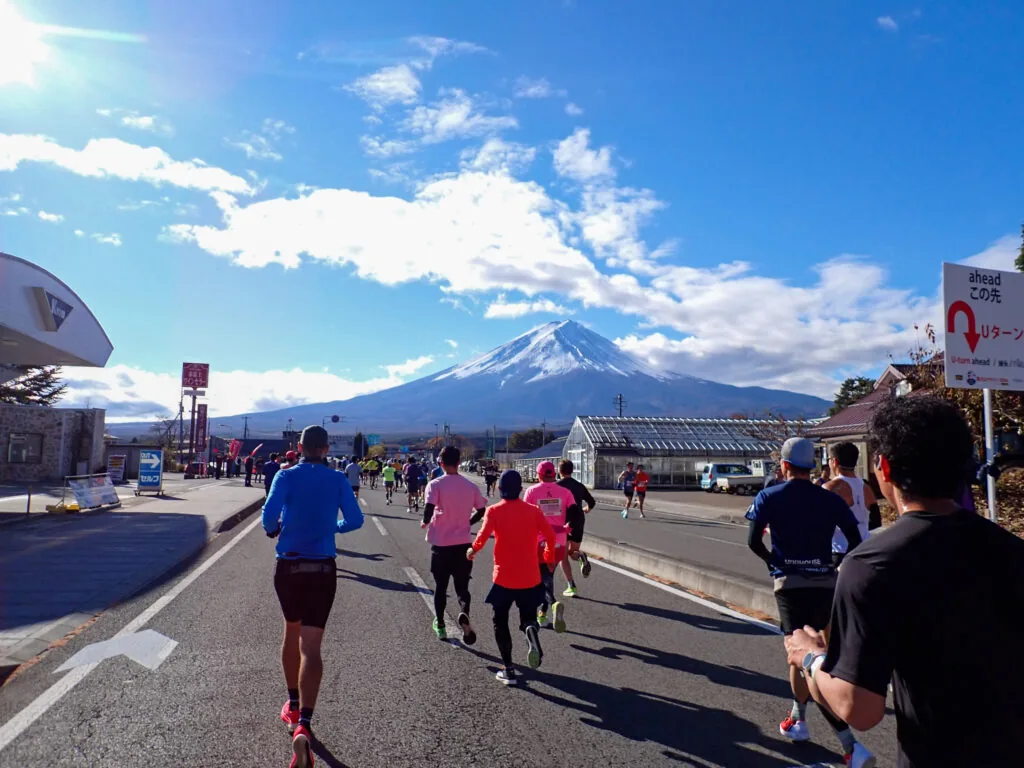 Uターンの案内標識が立つ道の先にそびえる富士山と、走るランナーたち