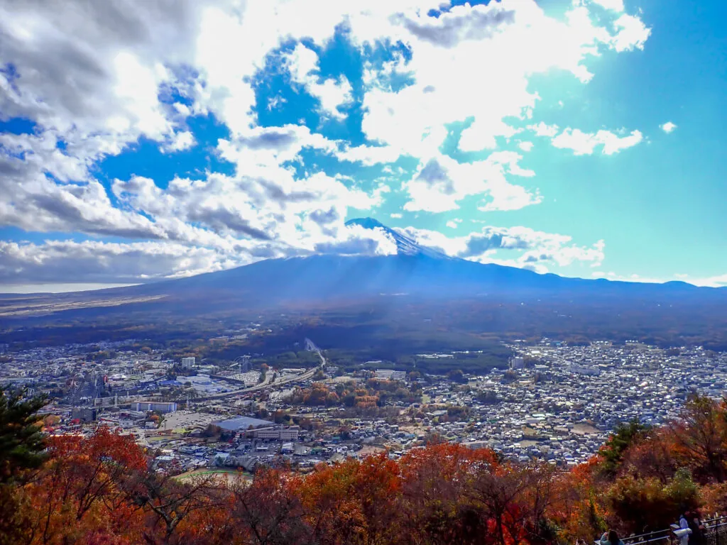 紅葉した木々越しに、街並みと雲のかかった富士山を見渡す眺め