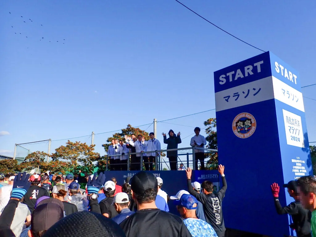 青い「START」の看板と、スタート台で手を振る人たち