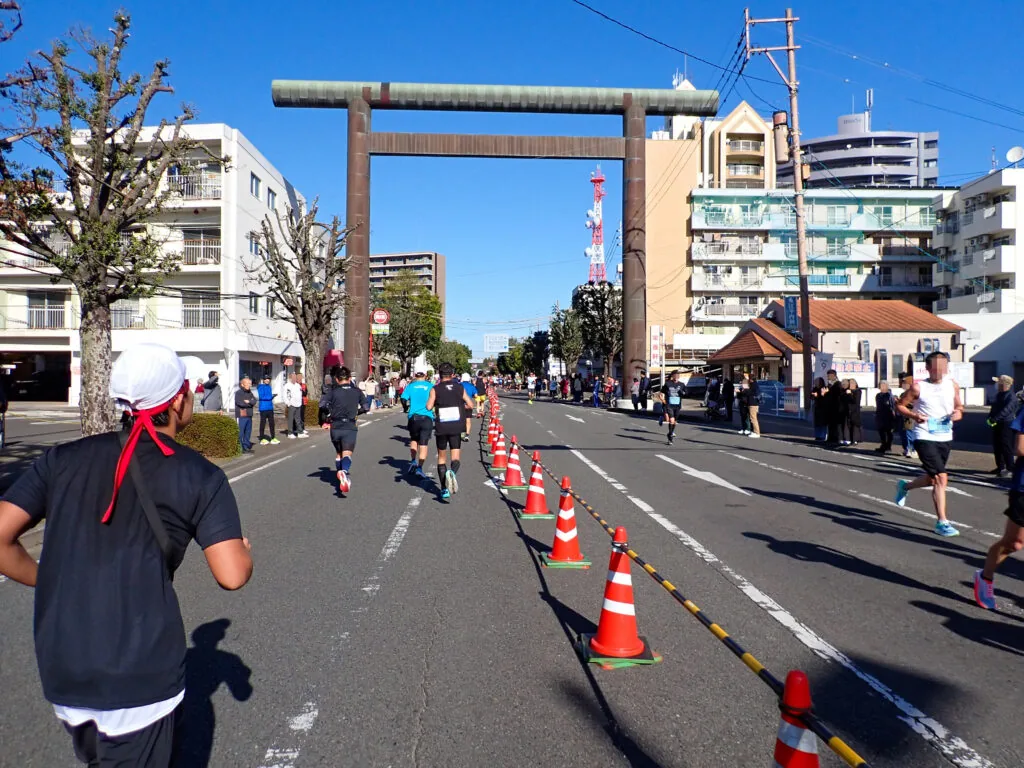 道路にまたがる宮崎神宮の大鳥居へ向かって走るランナーたちと、沿道の応援