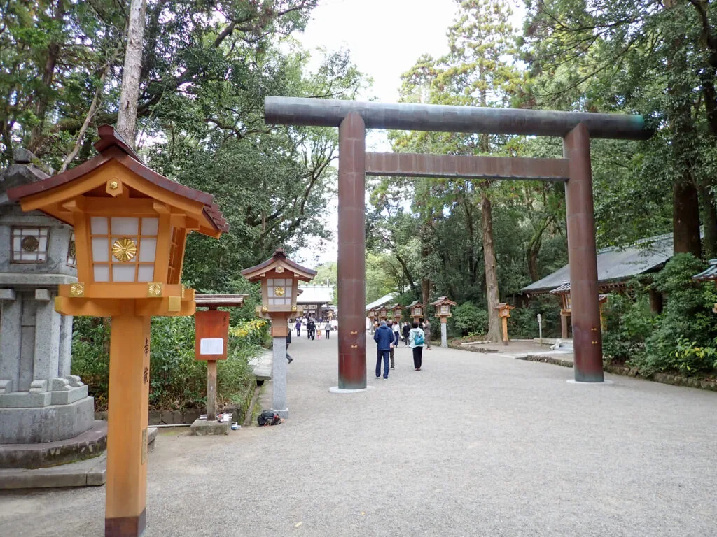 銅色の大きな鳥居と、木製の灯籠が並ぶ宮崎神宮の参道