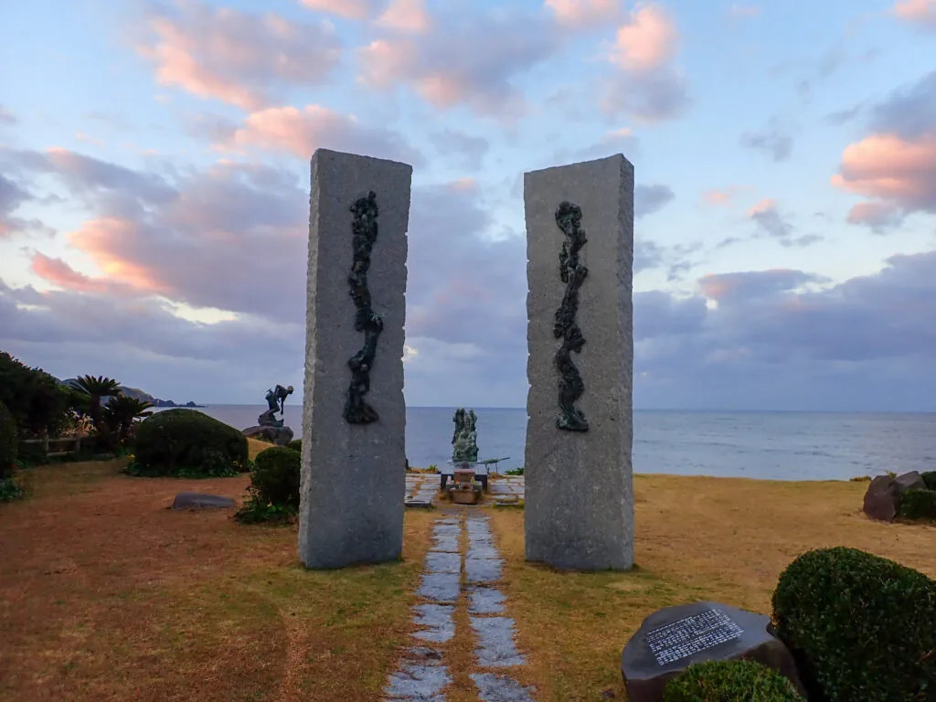 海に向かって立つ二本の石柱と、その奥の慰霊碑