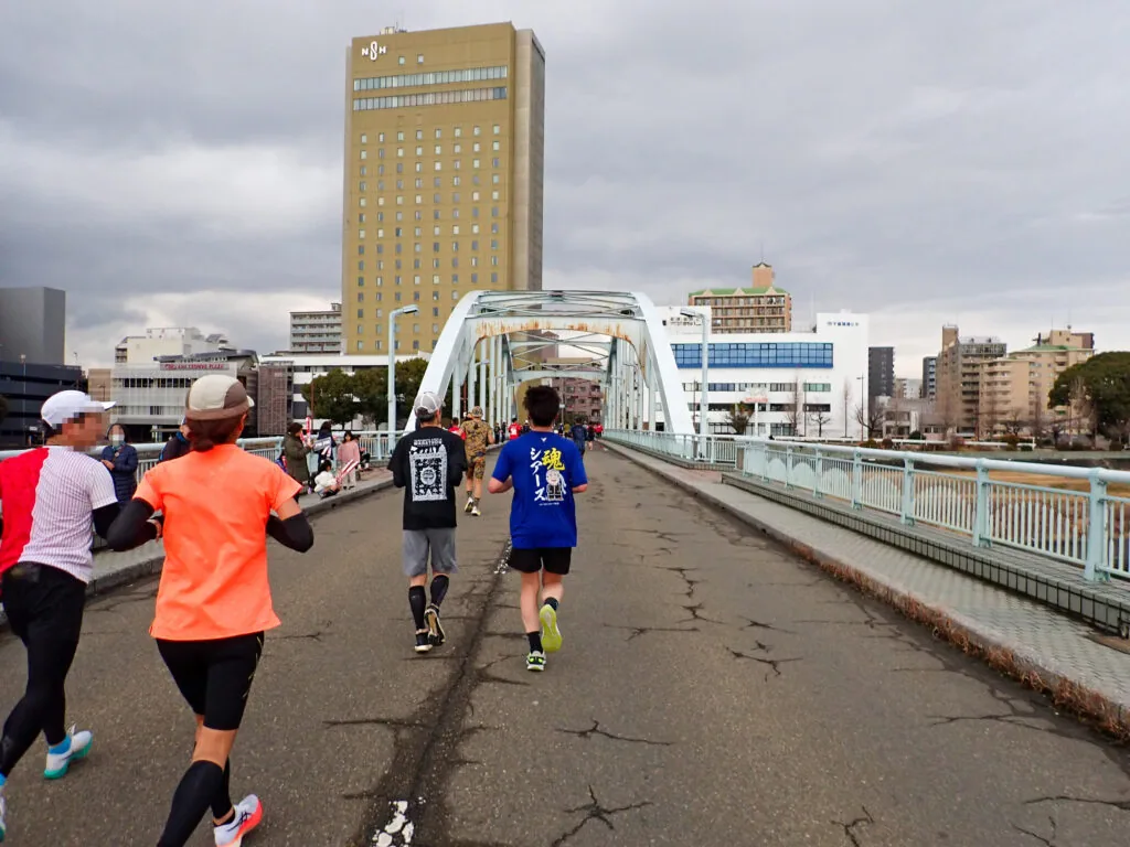 アーチ形の橋を渡るランナーと奥にそびえる高層ビル