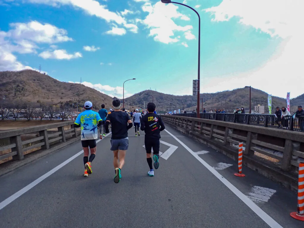 山並みを望む橋の上を進むランナーたち