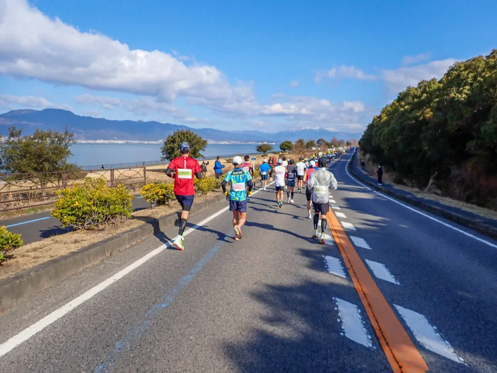 琵琶湖と山並みを望む湖岸の道を走るランナーたち