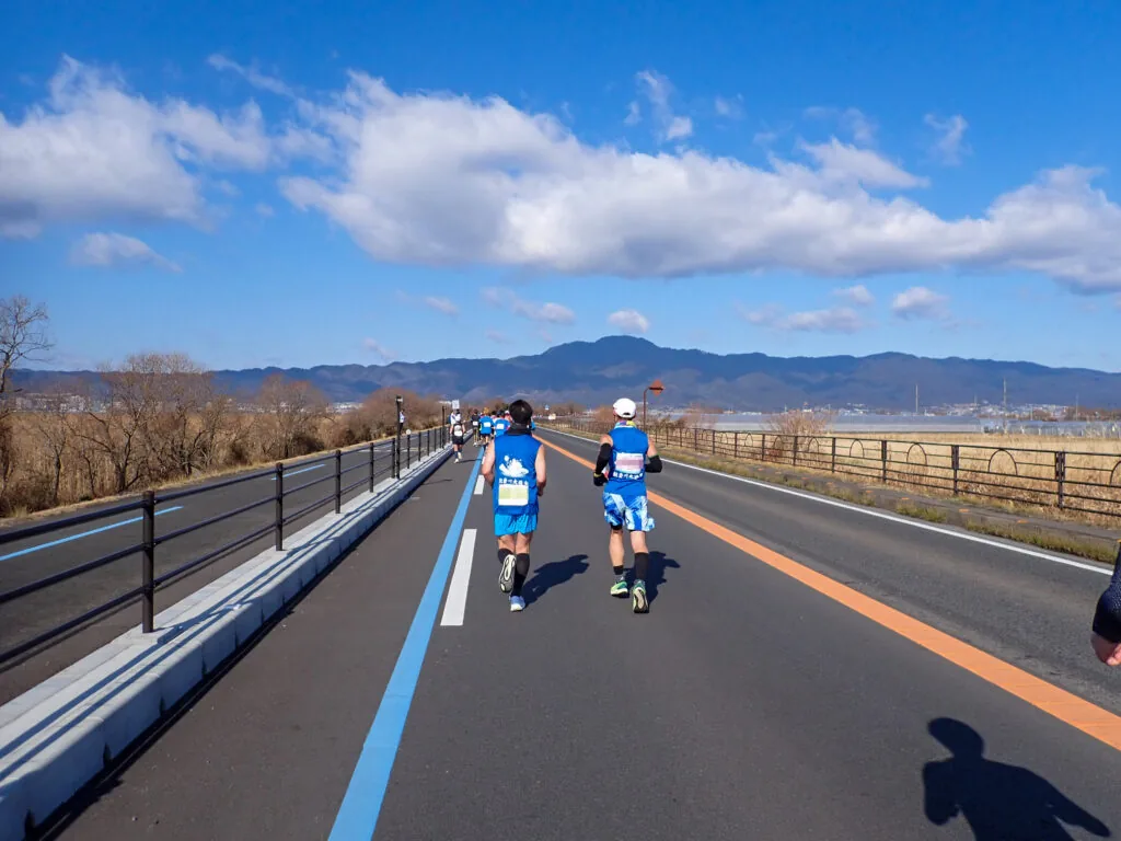 遠くに比叡山を望む湖岸道路を北上するランナーたち