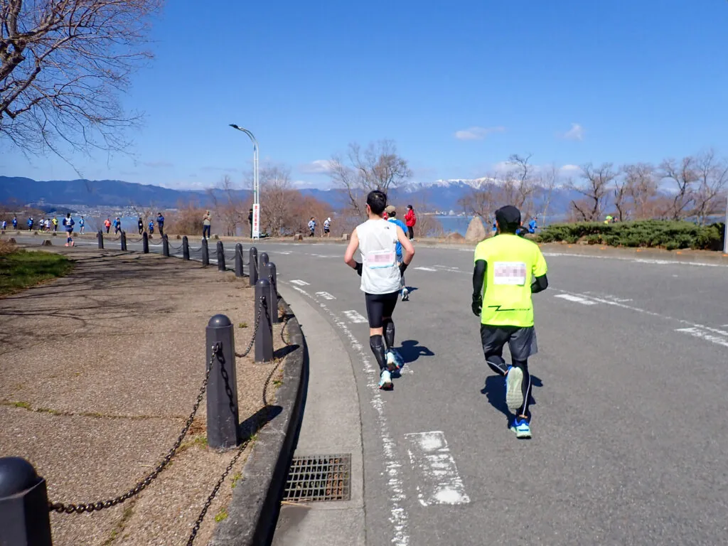 湖と雪山を望む烏丸半島の道を進むランナーたち
