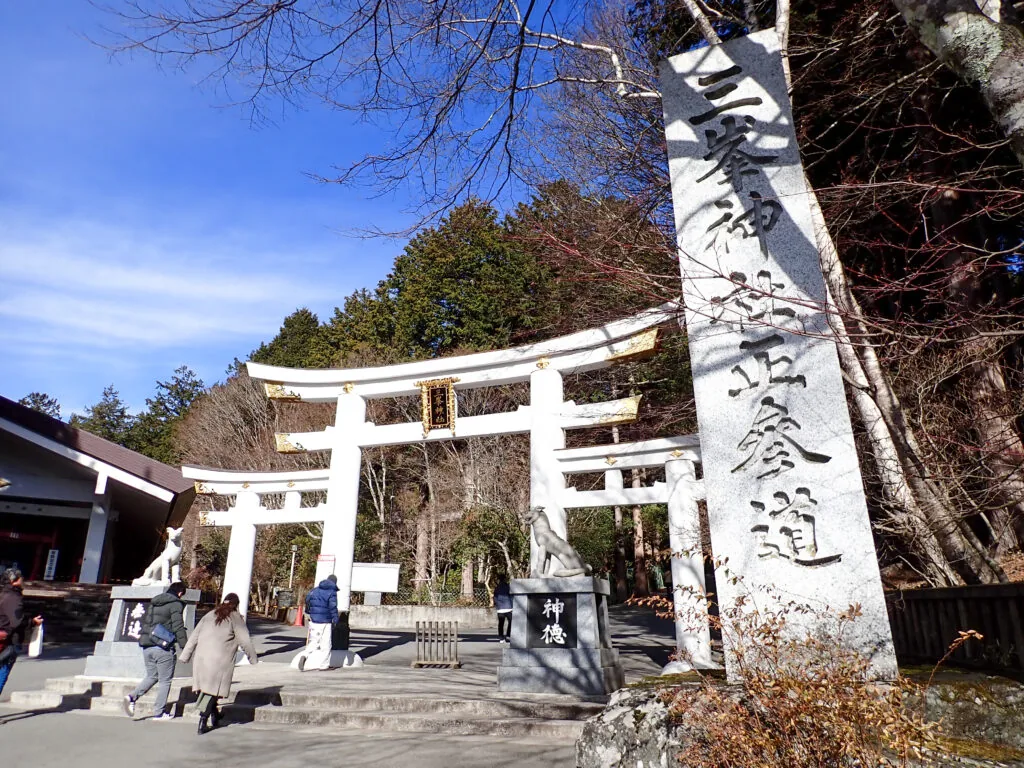 白い三ツ鳥居の脇に立つ三峯神社の参道の石柱