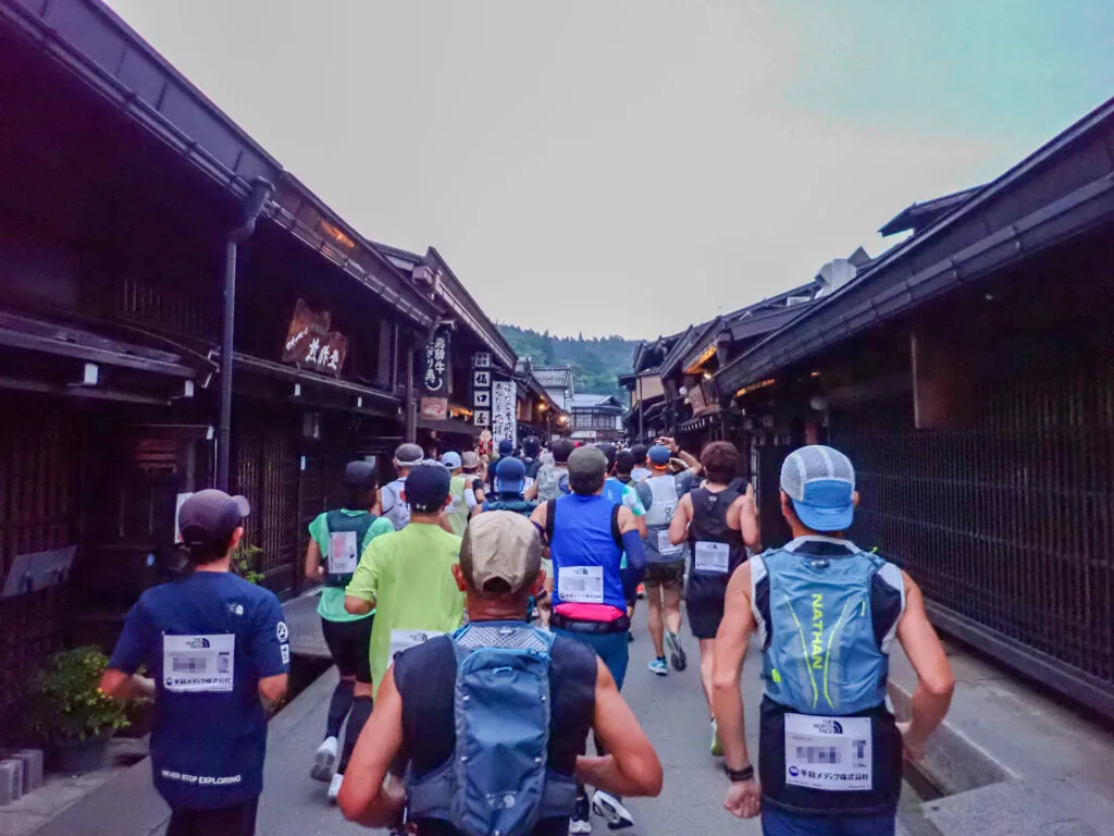 黒い木造の古い町家が並ぶ通りを走るランナーたち