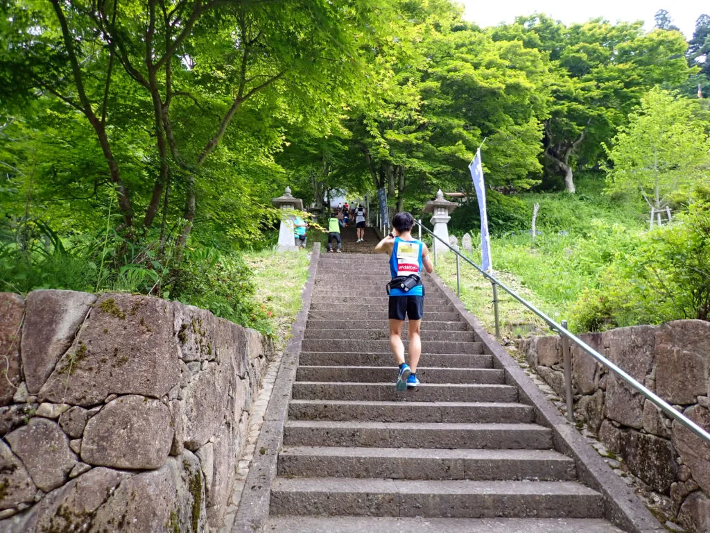 石垣の間を上へ続く千光寺の石段を上るランナー