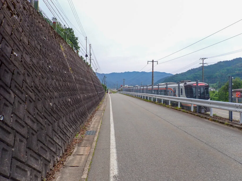 高い擁壁に沿って続く道と、奥を走る列車