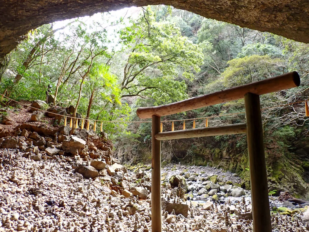 岩屋の奥に鳥居が立ち、河原に小石が積まれた天安河原