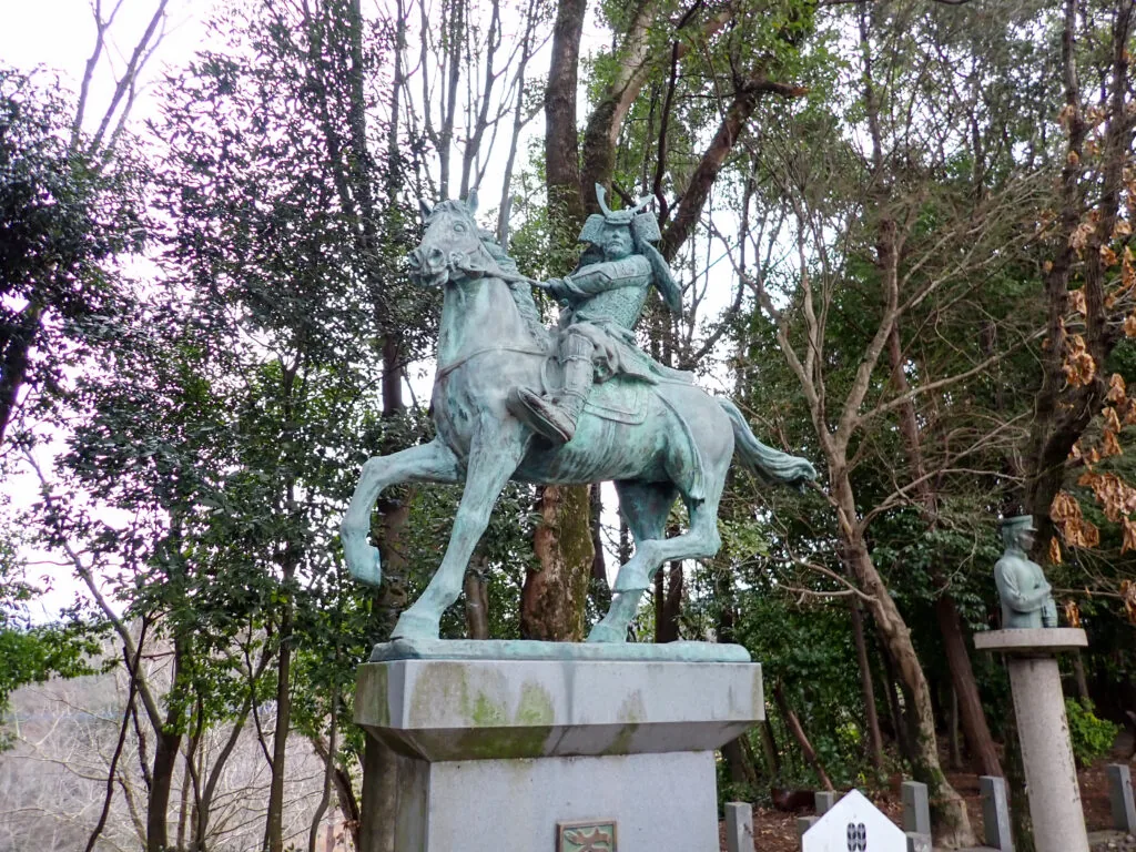 木立の中に立つ、馬にまたがる武将の銅像