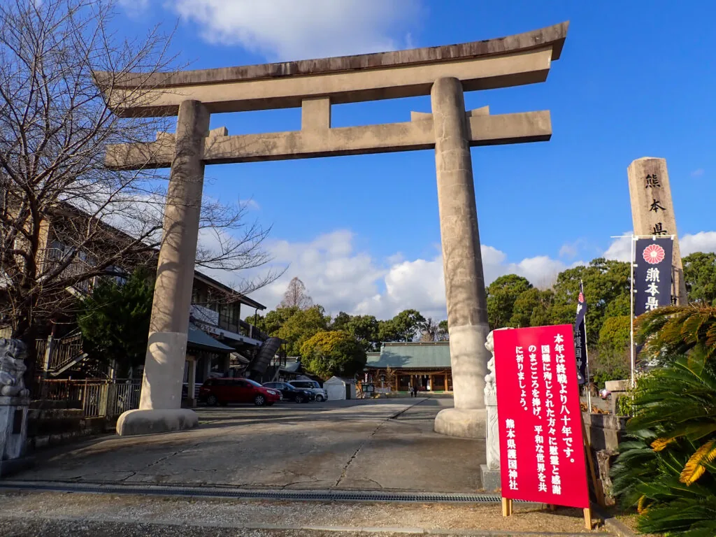 石の鳥居と赤い看板が立つ熊本縣護国神社の入口