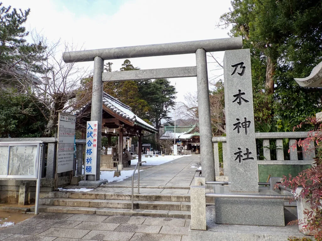 「乃木神社」の石柱と石の鳥居、雪が残る参道