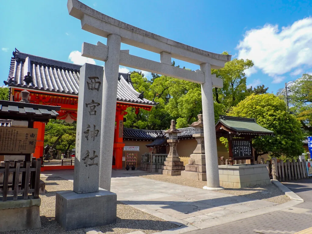 「西宮神社」の社号標と石の鳥居、奥に見える朱塗りの門