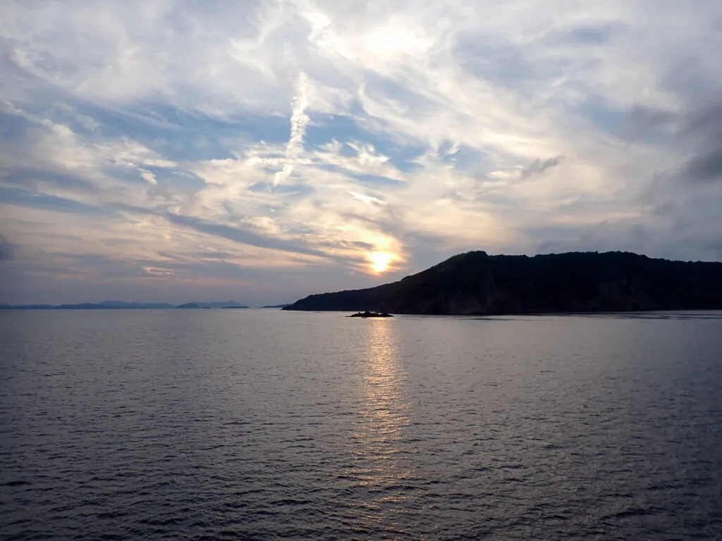 島影の向こうに夕日が傾く海