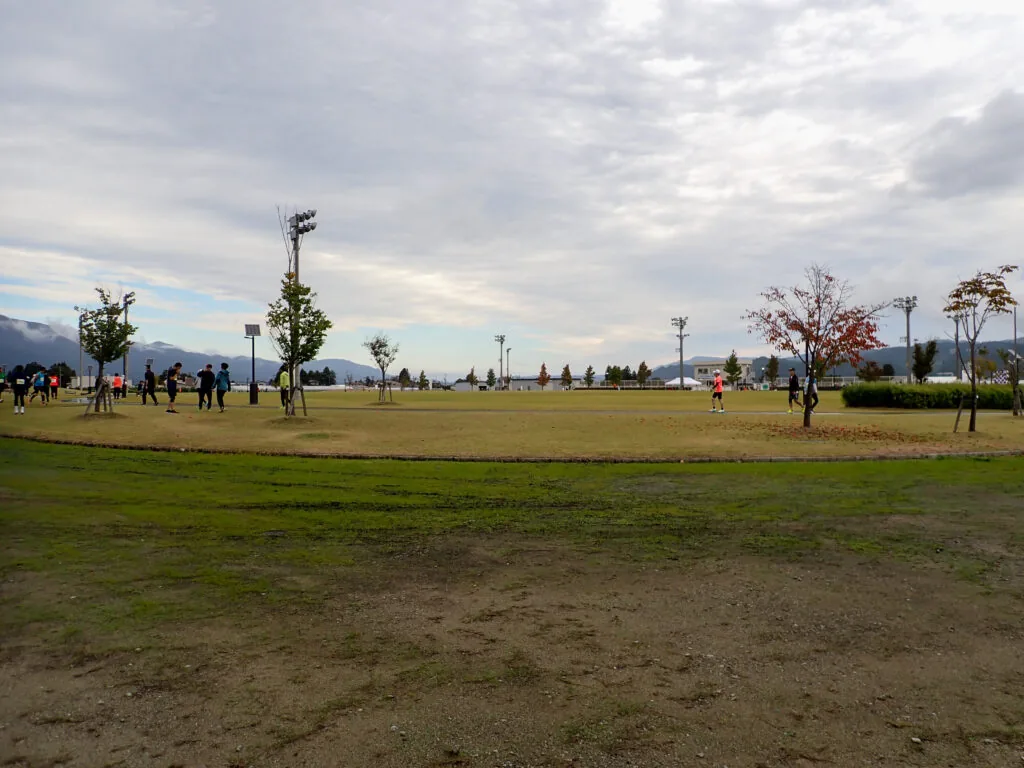 曇り空の下、山並みを望む長井市陸上競技場の芝生広場