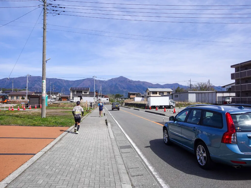 歩道を走るランナーと、住宅の向こうに連なる山並み