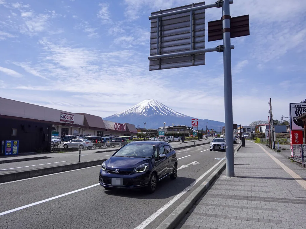 道路沿いの店舗の先に見える冠雪した富士山