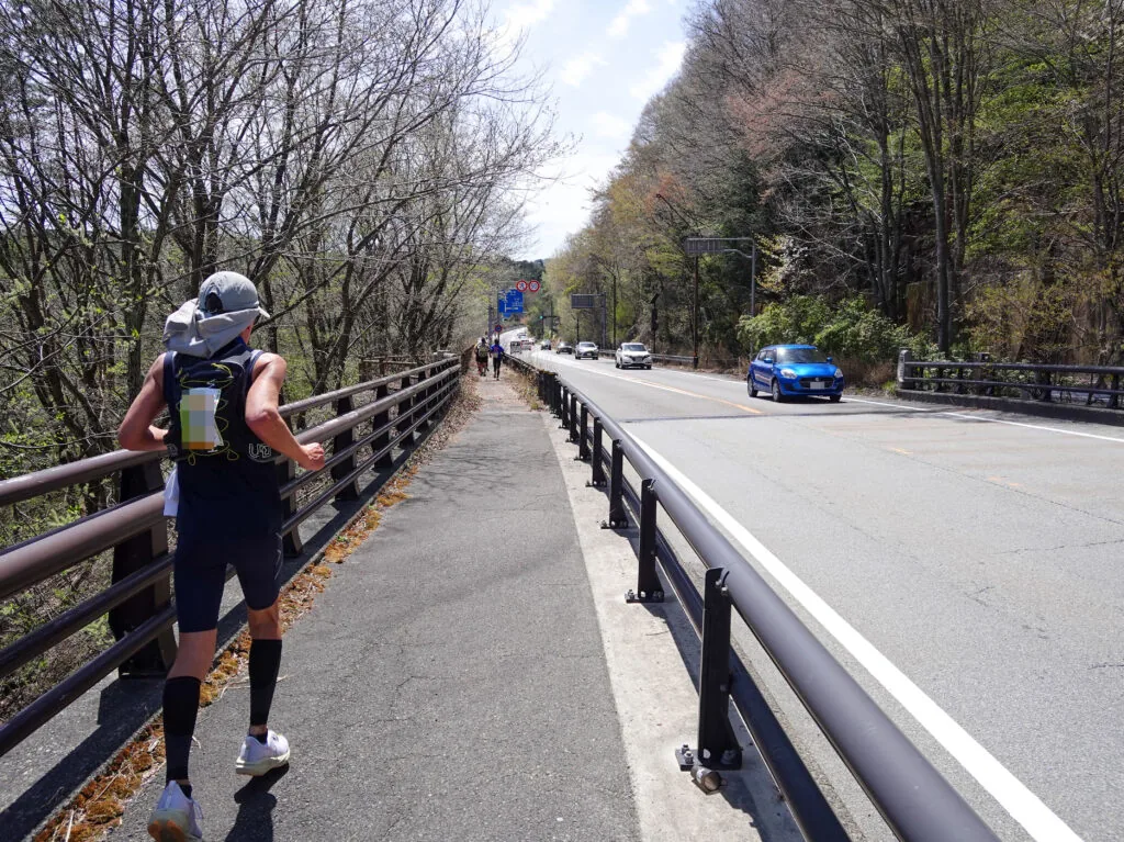 ガードレール沿いの歩道を走るランナーと木立