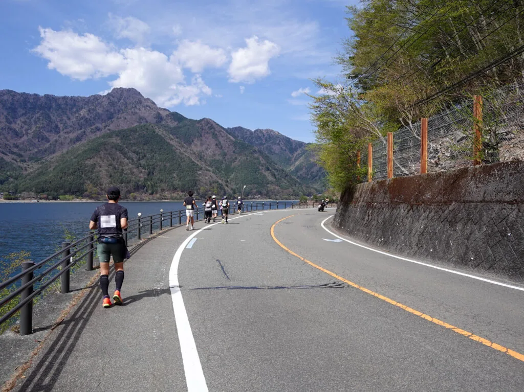 湖と山並みを望むカーブの道を走るランナー