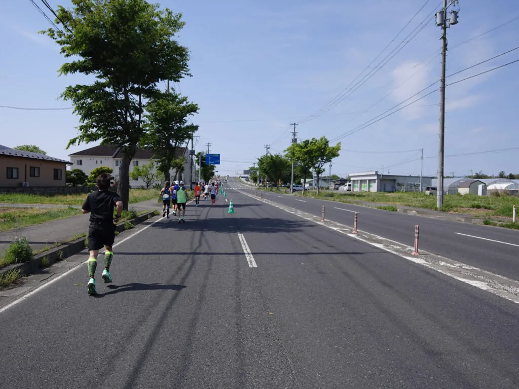 遠くまでまっすぐ続く道を走るランナーたち